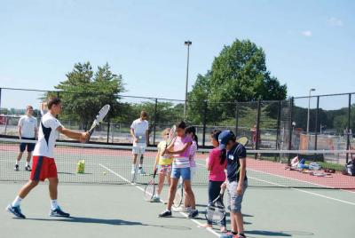 William Tarini (left), founder of the Kids Serving Kids Boston chapter, demonstrates tennis techniques for campers from the Holy Family Summer Enrichment Program.  Photo by Charlie Dorf